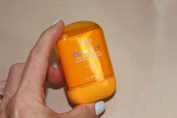 Hand holding the Anua Glow Stick sunscreen before applying