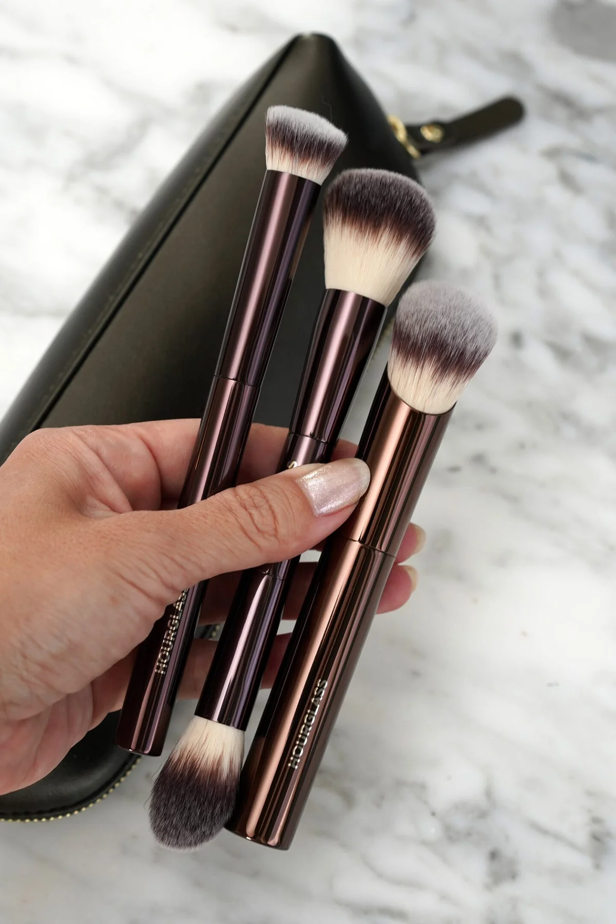 Three Hourglass makeup brushes in hand with black pouch