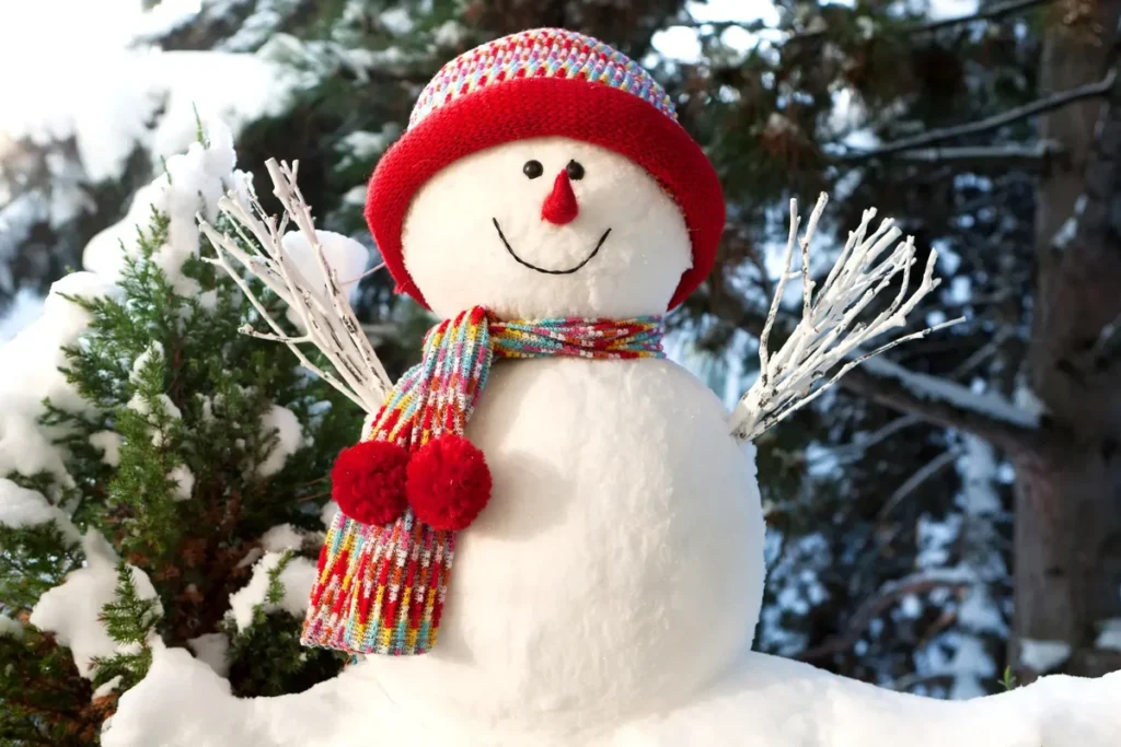 Handmade snowman in fresh snow with red hat and scarf