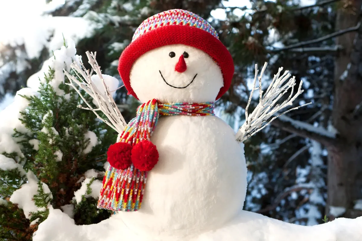 Handmade snowman in fresh snow with red hat and scarf