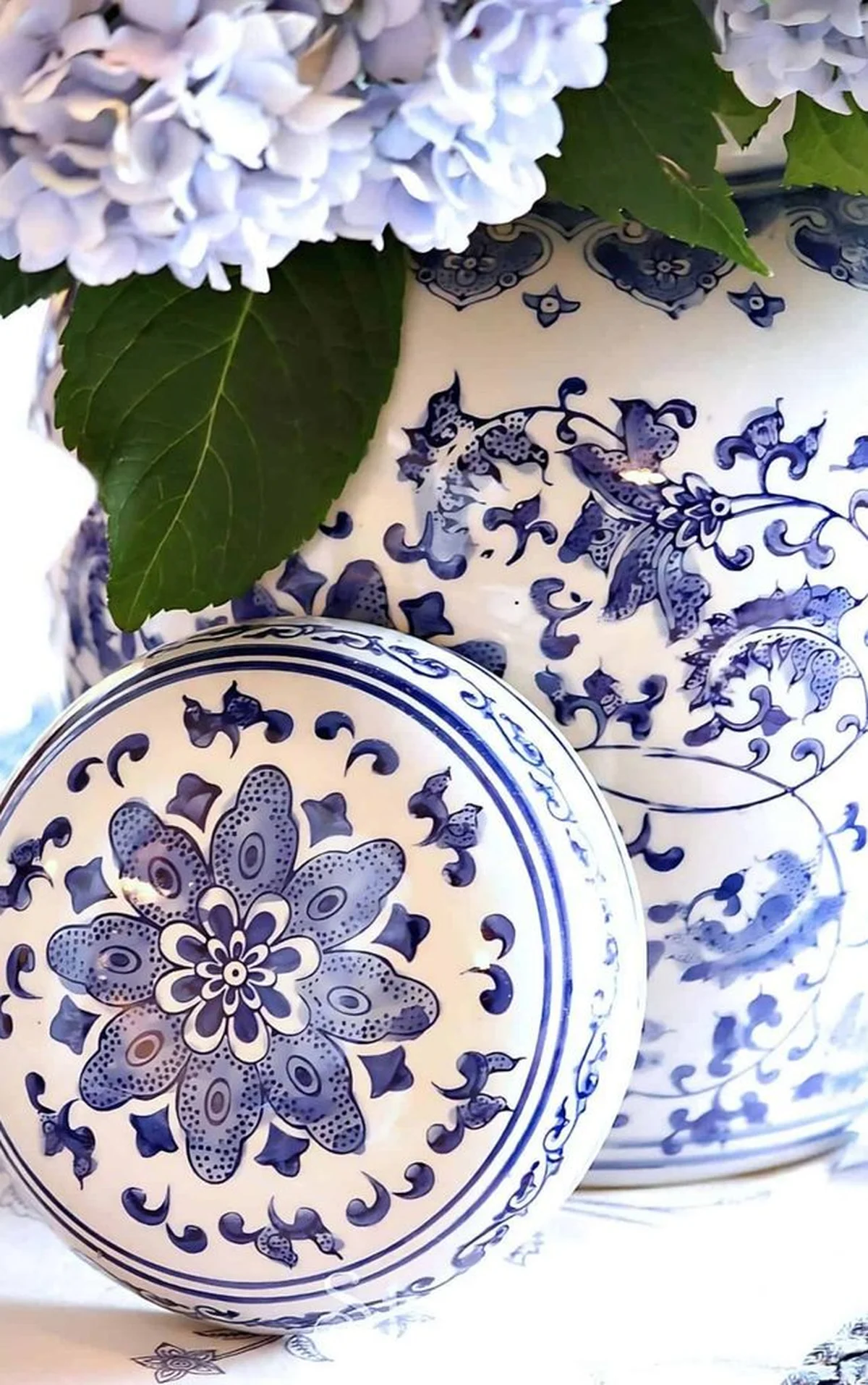 Blue hydrangeas beside ornate porcelain vase in soft morning light