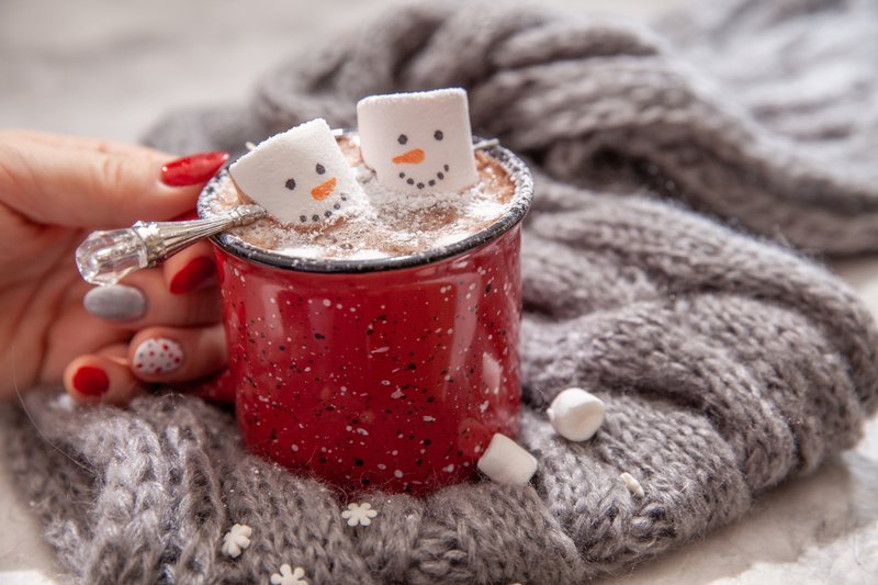 Hand holding hot cocoa mug with snowman marshmallows on knit blanket